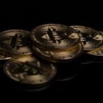 A close-up image of golden Bitcoin coins displayed on a reflective black surface.