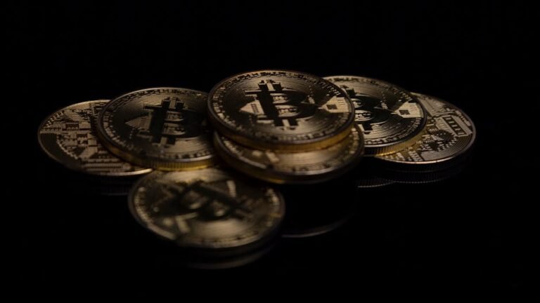 A close-up image of golden Bitcoin coins displayed on a reflective black surface.