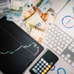 Overhead view of financial tools with Euro banknotes on a desk showing market trends and graphs.