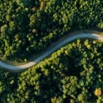 A winding road meanders through lush green forest from a high angle view.