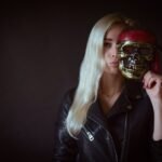 A woman in a leather jacket holds a skull mask, creating an eerie yet intriguing image.