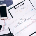 Stock market analysis setup with charts, phone, magnifier, and clipboards.
