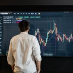 Back view of a trader analyzing cryptocurrency data on a monitor indoors.